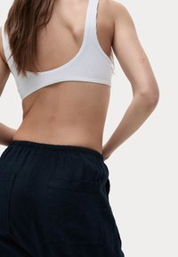 Bílá žebrovaná podprsenka s širokým zadním dílem, spárovaná s tmavými, volně střiženými kalhotami s kapsami na zádech a elastickým pasem.