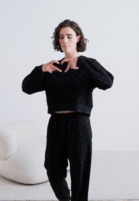 Set di loungewear nero con texture, composto da un pullover cropped con maniche lunghe e pantaloni con vita elastica, entrambi con un motivo geometrico.