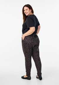T-shirt noir associé à des leggings en imprimé léopard marron foncé. Les leggings disposent d'une taille élastique et de poches latérales. Des ballerines noires complètent la tenue.