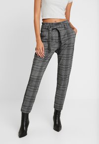 Černobílé kostkované kalhoty s elastickým pasem, bočními kapsami a zúženými nohavicemi. Stylizované s černými vysokými kotníkovými botami.