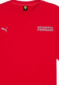Rød t-shirt med sølvfarvet "SCUDERIA FERRARI" tekst og et Puma-logo på venstre side. Ideel til racingsfans eller som casual wear.