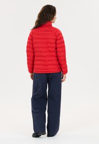 Rode pufferjack met een hoge kraag en horizontale stiksels. Gecombineerd met losse marineblauwe broek. De stof lijkt glad en geïsoleerd.