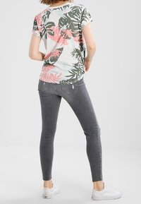 Kortärmad, ljus topp med grön och rosa tropisk bladmönster, ihop med grå skinny jeans och vita sneakers.