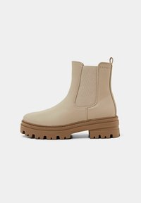 Bottine en cuir beige avec panneaux latéraux élastiques, semelle épaisse en caoutchouc marron, languette au talon et embossage discret de la marque près du col.