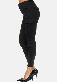 Schwarze Cargo-Hosen mit schlanker Passform, seitlichen Taschen, umgeschlagenen Säumen und einem Baumwoll-Mischgewebe; kombiniert mit glänzenden schwarzen High Heels.