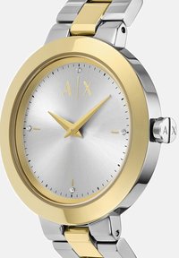 Sidabrinė ir auksinė nerūdijančio plieno apyrankė su apvaliu ciferblatu, auksiniais valandos ir minutės rodyklėmis bei deimanto akcentu 12 valandos pozicijoje.