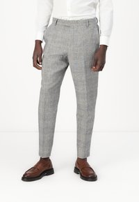 Grau karierte Hosen mit einem taillierten Schnitt, aus strukturiertem Stoff und flacher Frontgestaltung. Getragen mit braunen Loafers.