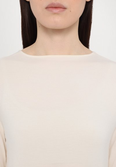 Top de culoare crem, cu o textură moale, cu decolteu rotund și fără cusături vizibile, evidențiind un design neted și minimalist.