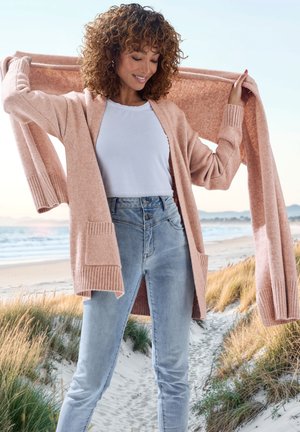 Helles rosa Cardigan aus weichem Strickstoff, mit offenem Vorderteil, gerippten Bündchen und Taschen, kombiniert mit hochgeschnittenen blauen Jeans.