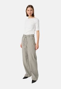 White, fitted, three-quarter sleeve top paired with high-waisted, wide-leg striped trousers in beige and grey, finished with black pointed shoes.