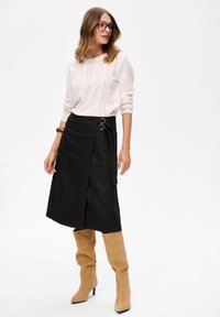 Zwarte denim wikkelrok met twee zijklanten, gecombineerd met een witte textuurtrui en beige knielange laarzen. Gladde stof, casual ontwerp.