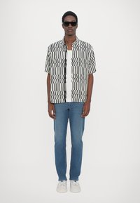 Short-sleeve shirt in black and white vertical stripes, worn over a white T-shirt, paired with light blue jeans and white sneakers.
