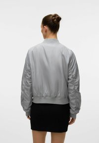 Grijze bomberjack met een cinched taille en elastische manchetten, met geplooide details op de mouwen, gedragen over een zwarte rok.