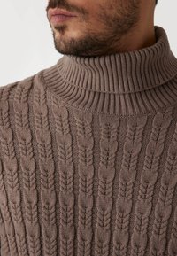 Gebreide coltrui in taupe. Kenmerkt een getextureerd kabelpatroon met een geribde kraag. Zachte stof textuur. Close-up van de halslijn en het patroon.