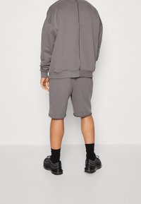 Szary bawełniany sweatshirt i dopasowane szorty, oba z surowymi krawędziami. Szorty mają wygodne dopasowanie, a cały zestaw zestawiono z czarnymi trampkami.