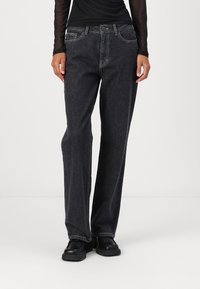 Black denim jeans with a straight cut, light stitching, five-pocket design, and a button closure. Worn with a fitted black long-sleeve top.
