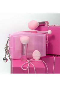 Roze make-up kwasten, een roze blend sponsje en een doorzichtige roze tas weergegeven op felroze geschenkdozen die vastzitten met een wit koord.
