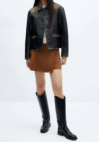 Czarna skórzana kurtka z widocznym szwem, brązowa zamszowa mini spódnica i czarne wysokie kozaki. Gładkie faktury z kontrastującymi kolorami.