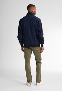 Marineblauwe bomberjack met hoge kraag, geribde manchetten en ritssluiting. Khaki broek en witte sneakers met een tan accent.