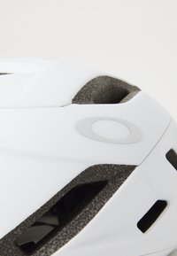 White bicycle helmet with textured dark gray accents and ventilation openings. Features a subtle logo on the side. Smooth surface finish.