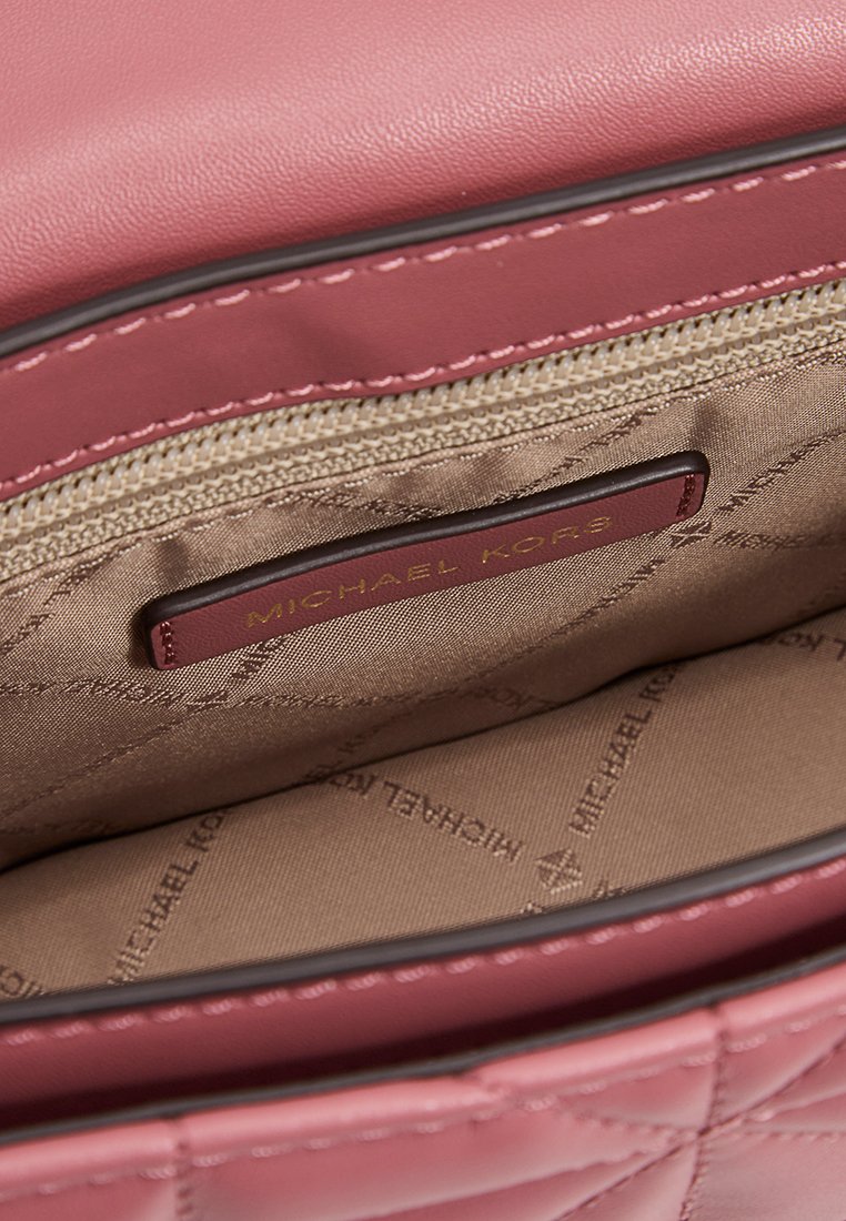 Intérieur d'un sac à main en cuir matelassé rose, avec une doublure beige, une étiquette de logo, une poche zippée et un design structuré.