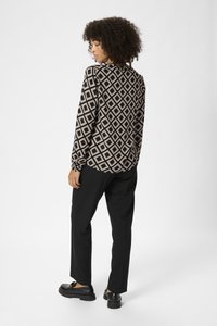Langärmlige Bluse mit einem schwarz-beigen Rautenmuster, kombiniert mit schwarzen Hosen und klobigen schwarzen Schuhen. Glatte Stoffqualität und lässiger Schnitt.