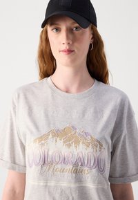 Pilkas trumpomis rankovėmis marškinėliai su kalnų grafika, kurioje parašyta "Koloradas" purpurinėmis ir auksinėmis raš letters, pagaminti iš medvilnės, su apvaliu kaklu.