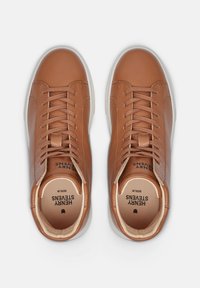 Sneaker in pelle marrone con tomaia texturizzata, punta arrotondata e suola in gomma bianca. Presenta lacci piatti e logo del marchio impresso sulla soletta.