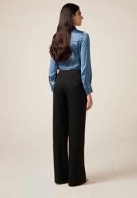 Blauw satijnen overhemd met lange mouwen en knoopmanchetten, gecombineerd met zwart, hooggetailleerd broek met krijtstreep en decoratieve accenten aan de achterkant.