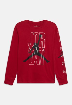 Rød langærmet skjorte med hvidt omrids af teksten "JORDAN" og en stor sort silhuet af en springende basketballspiller på fronten og ærmet.