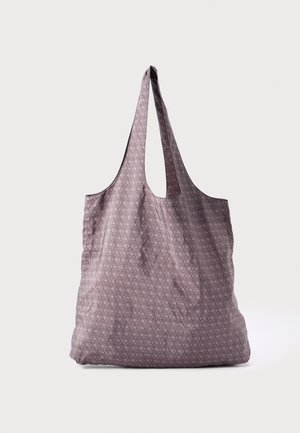 Violetti kangaskassi, jossa geometrinen kuvio, kaksi pitkää kahvaa ja pehmeä, rento muoto. Pinnan tekstuuri lisää yksityiskohtia.