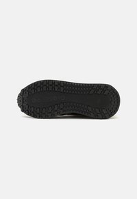 Suela de zapato de goma negra con textura, que presenta patrones circulares y rectangulares para un mejor agarre, además de un detalle en relieve del logo.