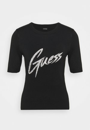Czarny krótki sweter z okrągłym dekoltem i dużym srebrnym brokatowym logo "Guess" na wysokości klatki piersiowej.