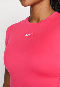 Top deportivo ajustado de color rosa, hecho de una tela suave, con cuello redondo y mangas cortas, que presenta un pequeño logotipo blanco de Nike en el pecho.