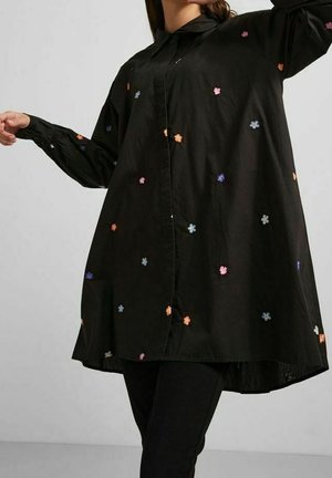 Camicia nera con bottoni, dal taglio rilassato, caratterizzata da un ricamo floreale colorato su tutta la superficie. Maniche lunghe e orlo curvo con spacchi laterali.