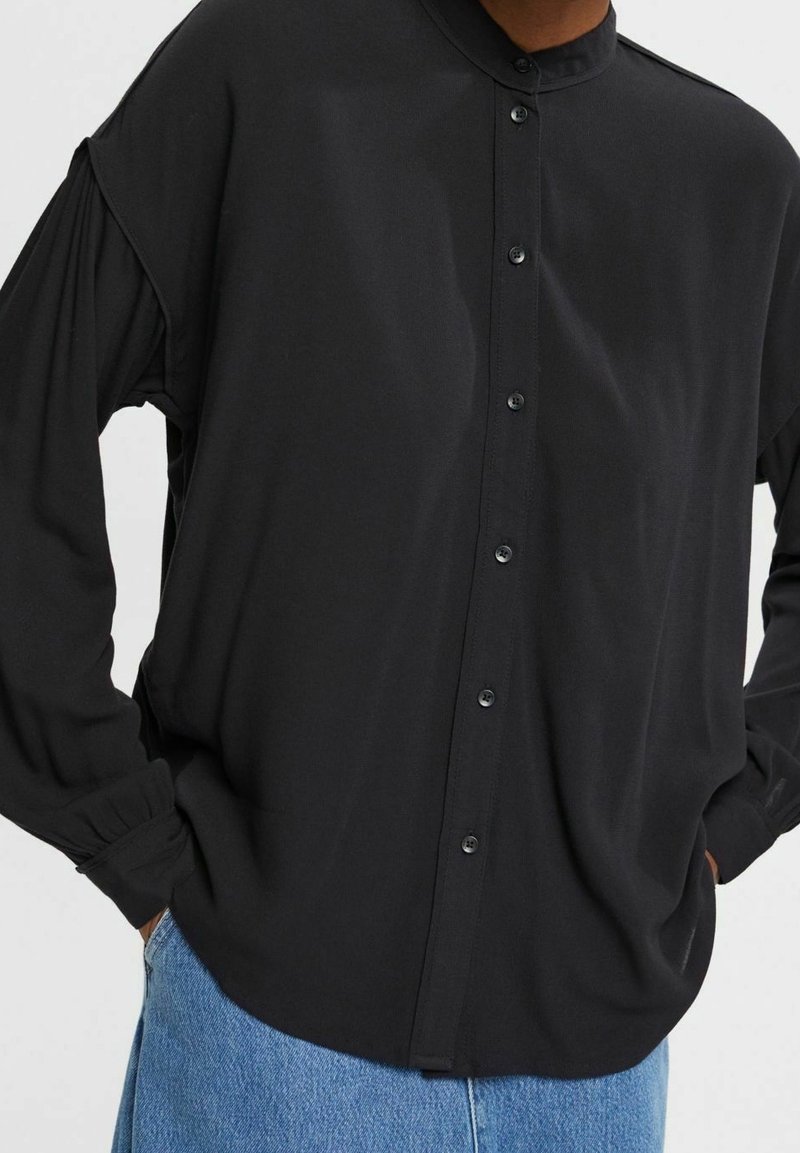 Camisa negra de botones con cuello mandarín, corte holgado y mangas fruncidas. Confeccionada en una tela suave con un diseño minimalista.