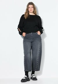 Suéter negro de punto de gran tamaño con detalles recortados, combinado con jeans de pierna ancha de color gris oscuro con tachuelas plateadas en los laterales. Zapatos de plataforma negros.