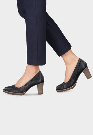 Musta nahkasaappaat, joissa on korkea korko, rei'itetty muu design, pyöreä varvas ja teksturoitu vaaleanruskea paksukorko. Yhdistetty tummansinisiin housuihin.