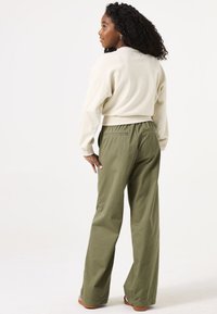 Lichtbeige cropped sweatshirt en olijfgroene wijde broek met elastische tailleband; heeft achterzakken en een relaxte pasvorm.