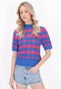 Niebieski i różowy sweter dzianinowy z krótkim rękawem, z poziomym wzorem w paski oraz ściągaczami u rękawów i u dołu, noszony z postarzanymi szortami dżinsowymi.