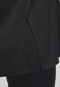 Black athletic top with a textured fabric, featuring a side slit and stitched hems, paired with black leggings.