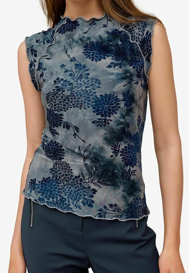 Ærmeløs top i gennemsigtig, mønstret stof med marineblå blomsterdesigns på en afdæmpet grå baggrund; bølgede kanter og blød tekstur.