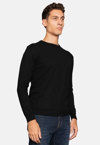 Black knit sweater with a classic round neckline, long sleeves, and ribbed cuffs. Worn with blue jeans, smooth texture, and fitted design.