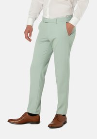 Hellgrüne maßgeschneiderte Hose mit Seitentaschen, glatter Textur und geradem Bein, kombiniert mit braunen Lederschuhen.