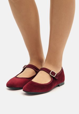 Scarpe Mary Jane in suede bordeaux con punta arrotondata, sottile cinturino e dettaglio della fibbia rettangolare, dotate di suola piatta e morbida al tatto.