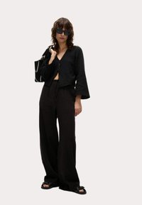 Czarna krótka bluzka z szerokimi rękawami, zestawiona z luźnymi czarnymi spodniami. Akcesoria to czarna torba i ciemne okulary przeciwsłoneczne.