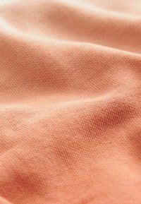 Miękka brzoskwiniowa tkanina o delikatnej strukturze, z subtelnym wzorem prążkowym, swobodnie układa się w nierówne fałdy. Idealna do wygodnych ubrań.