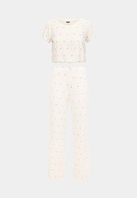 Κοντομάνικο κοντό τοπ κρεμ και αντίστοιχο παντελόνι, και τα δύο με μικρά ροζ σχέδια καρδιάς. Ελαφρύ, ελαστικό ύφασμα με ριμπ υφή και κυματιστά τελειώματα.