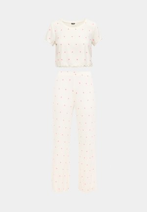 Κοντομάνικο κοντό τοπ κρεμ και αντίστοιχο παντελόνι, και τα δύο με μικρά ροζ σχέδια καρδιάς. Ελαφρύ, ελαστικό ύφασμα με ριμπ υφή και κυματιστά τελειώματα.