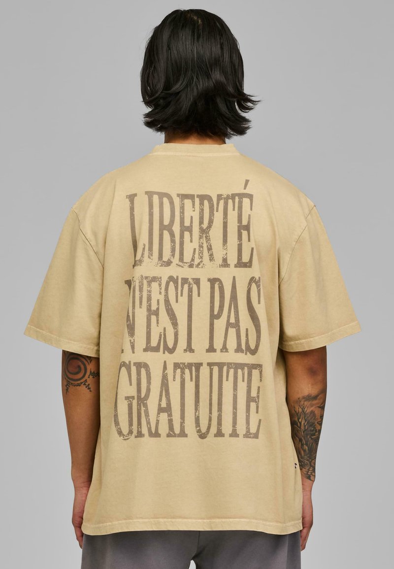 Tricou oversized bej cu mâneci scurte, având imprimat îndrăzneț și uzat textul "LIBERTÉ N'EST PAS GRATUITE" pe spate. Material din bumbac.
